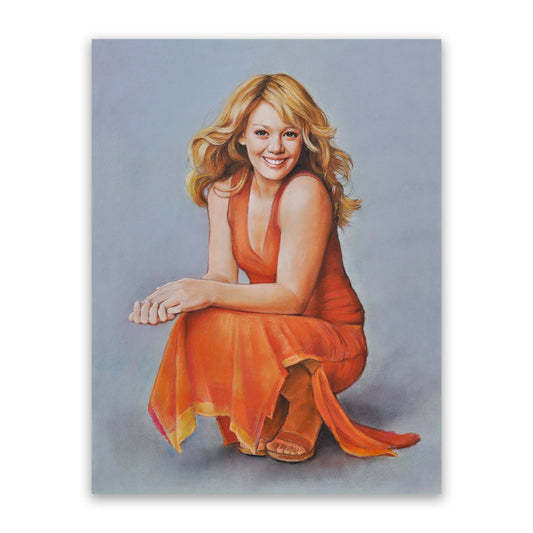 Pastel portrait of a beautiful, fair-skinned woman with dark eyes, wearing an orange dress. The woman has blonde, wavy hair and brown eyes. The dress has a v-neck, wide straps, a slit in the long skirt.  The woman is posing in a crouching position, bare arms placed on her knees. She is smiling at the camera. The portrait has a gray background. She is smiling at the camera.